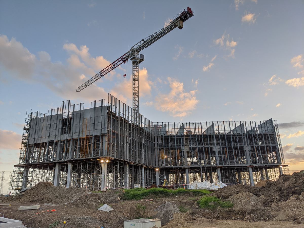 Steel frame of a multistorey building under construction at dusk, with a tower crane above it